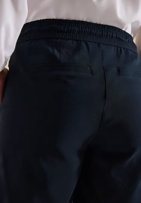 Rückansicht einer Person in dunkelblauen, elastischen Freizeithosen mit Händen in den Taschen.