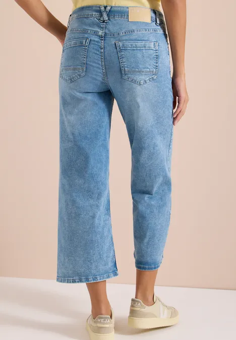 Achteraanzicht van een persoon in losse, lichte, enkellange jeans met sneakers.