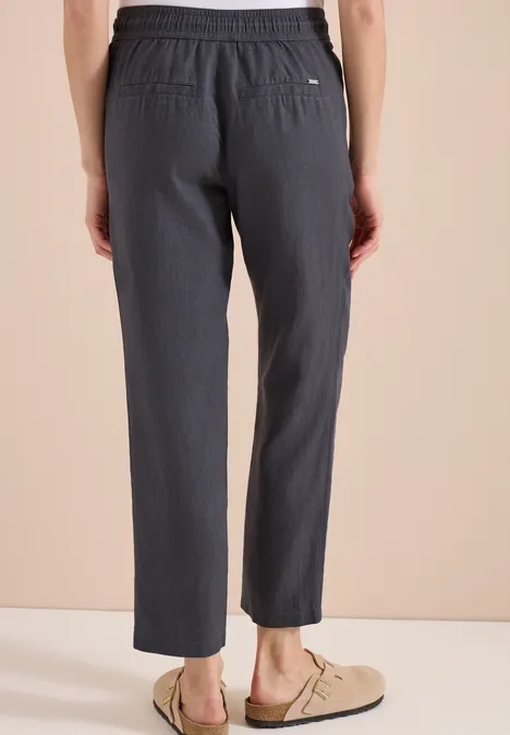 Achteraanzicht van een persoon met grijze, loszittende broek en beige instapschoenen.