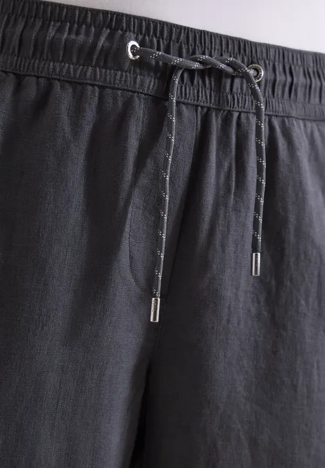 Zwarte broek met elastische taille en trekkoord, lichte structuur met subtiele lijnen, zilverkleurige koorduiteinden.