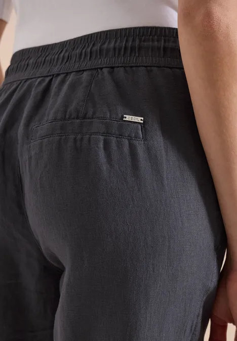 Achteraanzicht van persoon in donkergrijze linnen broek met elastische taille en achterzak met metalen logo