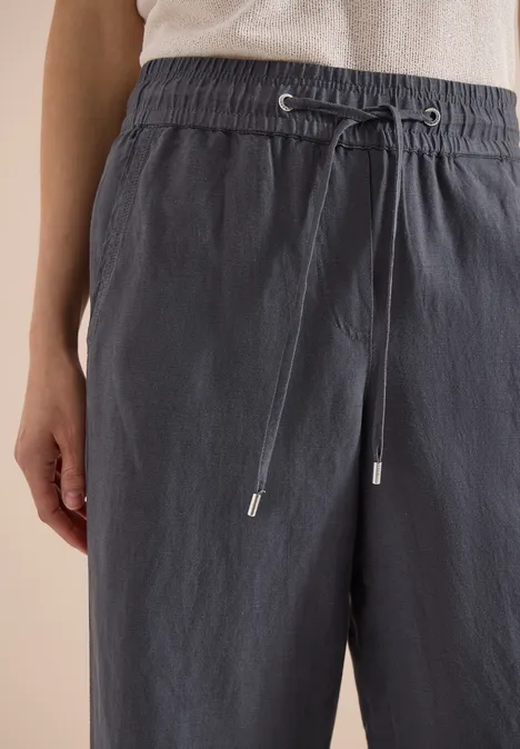 Graue, lockere Leinenhose mit Kordelzug in der Taille, getragen von einer Person.