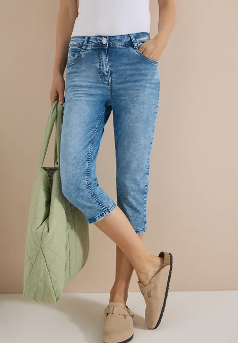 High waist Slim Fit Capri Jeans authentic used wash Eine Person trägt hellblaue, knielange Jeans, einen weißen Top, eine grüne Tasche und beige Mokassins.