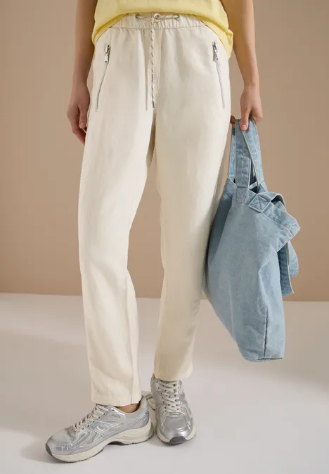 Personne porte un pantalon blanc, des baskets grises et tient un sac bleu clair.