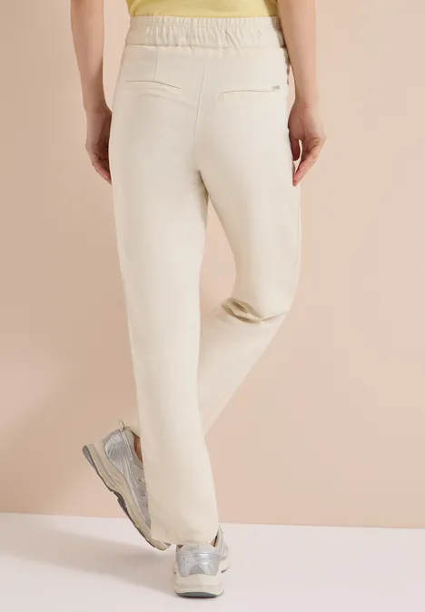 Vue arrière d'une personne en pantalon de jogging clair et baskets argentées sur fond neutre.
