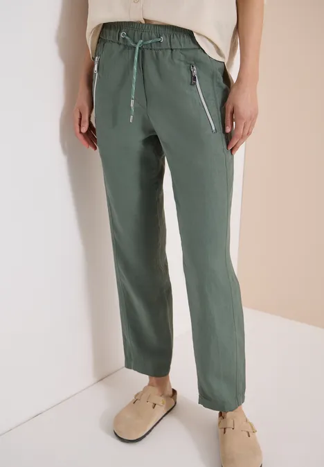 Damen-Hose in Olivegrün mit Kordelzug und Reißverschlusstaschen, getragen mit beigen Clogs.