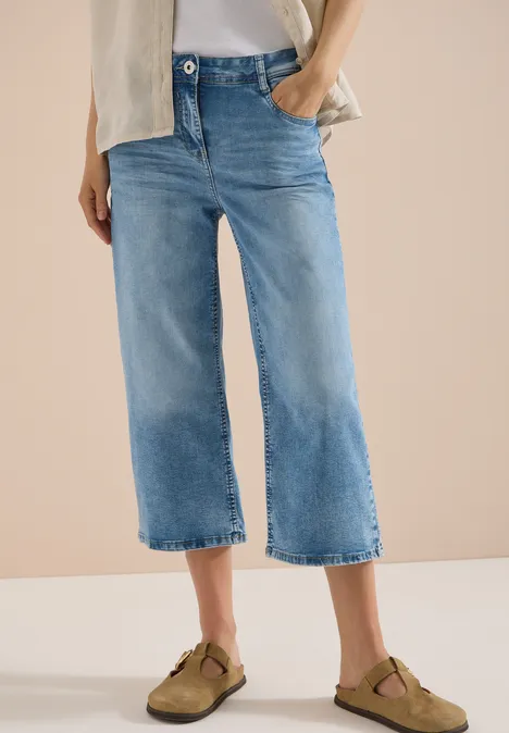 3/4 High Waist Wide Leg Jeans im Slim Fit light blue washed Frau trägt hellblaue, weite Cropped-Jeans und braune Clogs.
