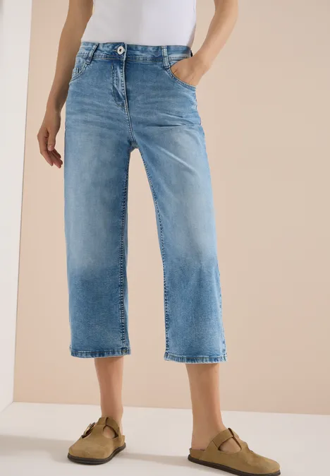 3/4 High Waist Wide Leg Jeans im Slim Fit light blue washed Eine Person trägt hellblaue Culotte-Jeans und beige Slipper vor neutralem Hintergrund.