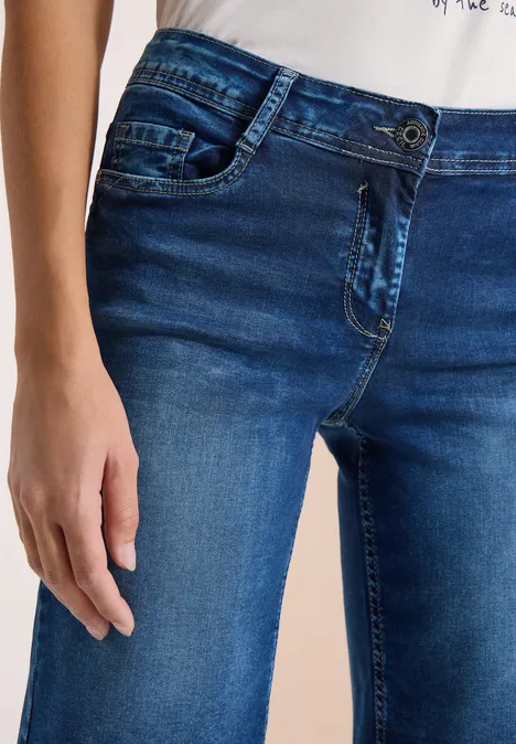 Een persoon draagt een blauwe spijkerbroek, zichtbaar van heup tot bovenbeen, hand ontspannen langs het lichaam.