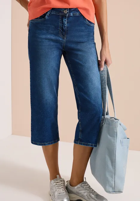 Pantalon en jean bleu foncé mi-long à jambes larges, associé à des baskets blanches et un sac bleu clair.