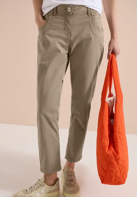 Person trägt olivgrüne Hose und hält orangefarbene Einkaufstasche.