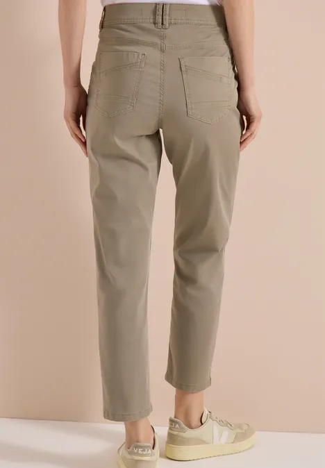 Frau von hinten in khakifarbener High-Waist-Hose mit aufgesetzten Taschen und hellen Sneakers.