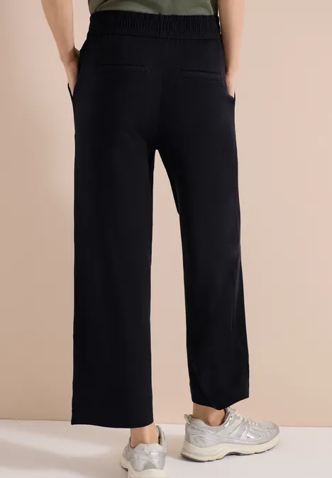 Schwarze, gerade geschnittene Hose mit aufgesetzten Taschen und elastischem Bund, kombiniert mit sportlichen Sneakern.