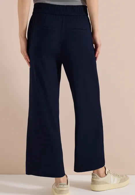 Achteraanzicht van een donkerblauwe wijde broek met elastische tailleband, achterzakken en sneakers.