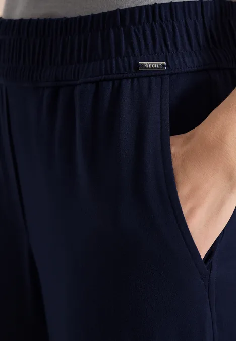 Close-up van een donkerblauwe broek met elastische taille en zijzak, hand in de zak.
