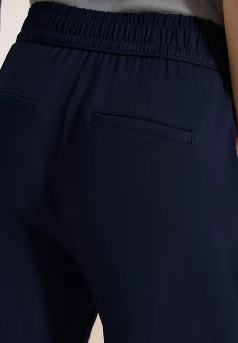 Achteraanzicht van persoon in donkerblauwe broek met elastische tailleband en twee achterzakken.