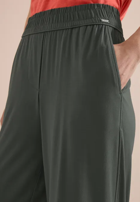 Donkergroene, loszittende broek met elastische tailleband en zijzakken.