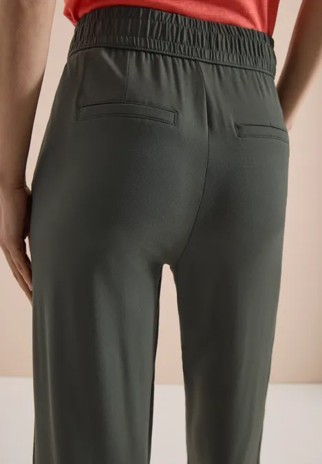 Een persoon van achteren in donkergroene joggingbroek met elastische taille en achterzakken tegen lichte achtergrond.