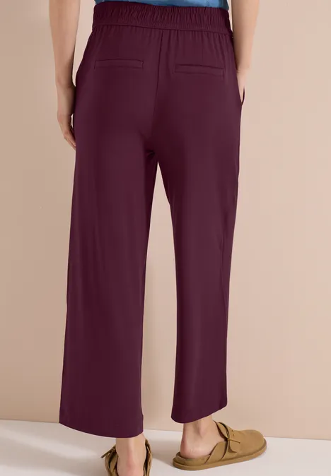 Rückenansicht einer weiten, brombeerfarbenen Hose mit Gummibund und zwei Gesäßtaschen, kombiniert mit Mokassins.