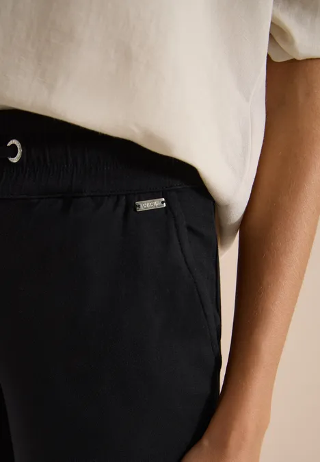 Close-up van torso in wit T-shirt en zwarte elastische broek met zak.