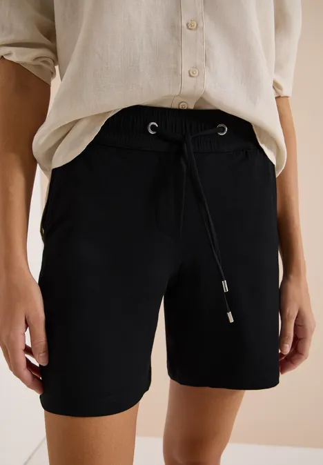 Zwarte, knielange short met trekkoord, gecombineerd met een los, licht shirt.