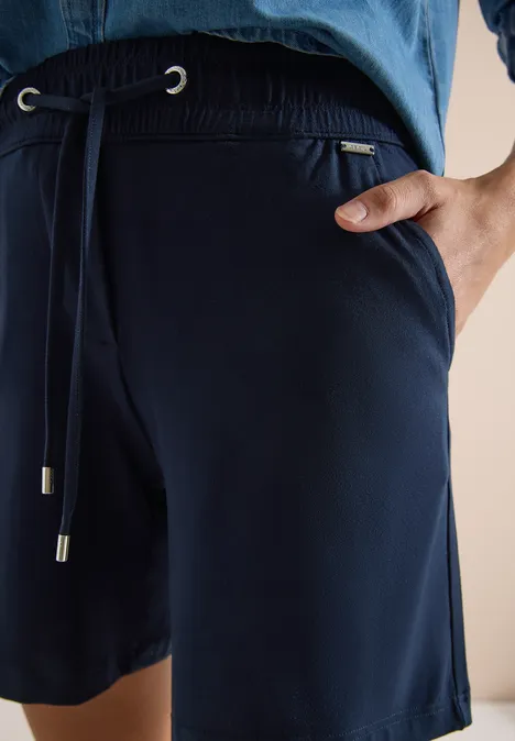 Close-up van donkerblauwe jersey short met trekkoord en steekzak aan de zijkant.