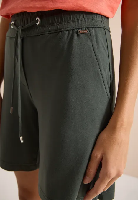 Close-up van een donkergroene short met trekkoord en hand langs de dij.