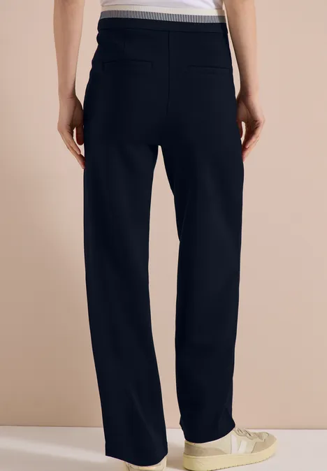 Person von hinten in weiten schwarzen Hosen und weißen Sneakern.