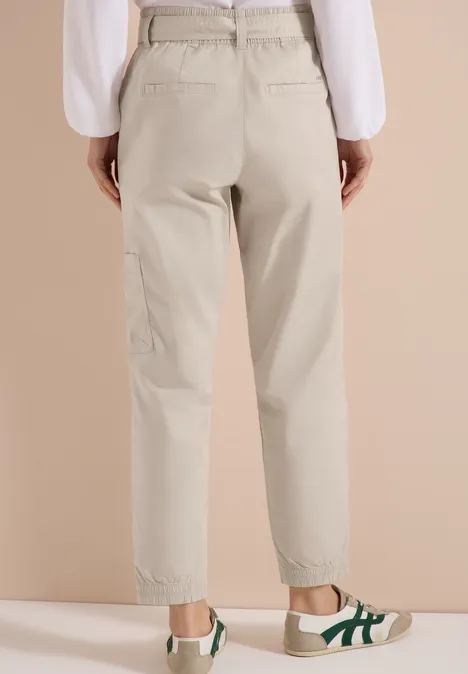 Beige Geradehose mit hohem Bund und elastischem Abschluss, dazu weiße Sneaker mit grünen Details.