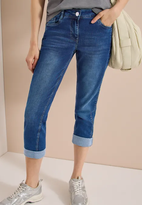Mid Waist straight leg jeans in casual fit mid blue wash Een persoon draagt donkerblau capri-jeans, lichtgrijze sneakers en een lichte schoudertas.