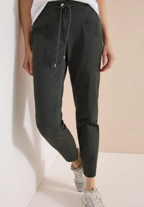 Mid Waist Slim Legs broek in een gewassen look clear khaki Donkergroene joggerbroek met trekkoord, zakken en boorden, gecombineerd met grijze sneakers.