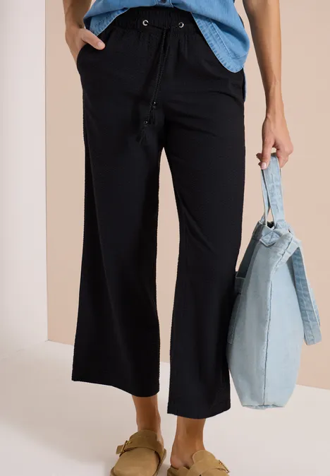 Zwart wijde 3/4-broek met trekkoord, gecombineerd met lichtblauwe tas en sandalen.