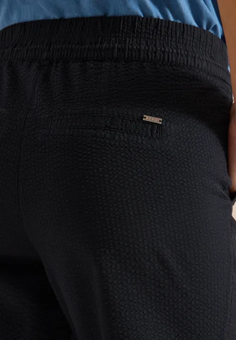 Achteraanzicht van iemand in een zwarte, gestructureerde broek met een ritszak aan de achterkant.