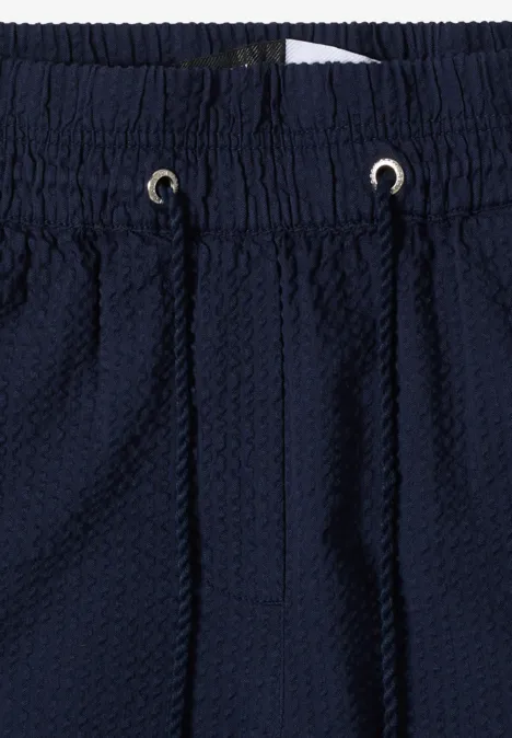 Close-up van een donkerblauwe, gestructureerde broek met elastische tailleband en aantrekkoord.