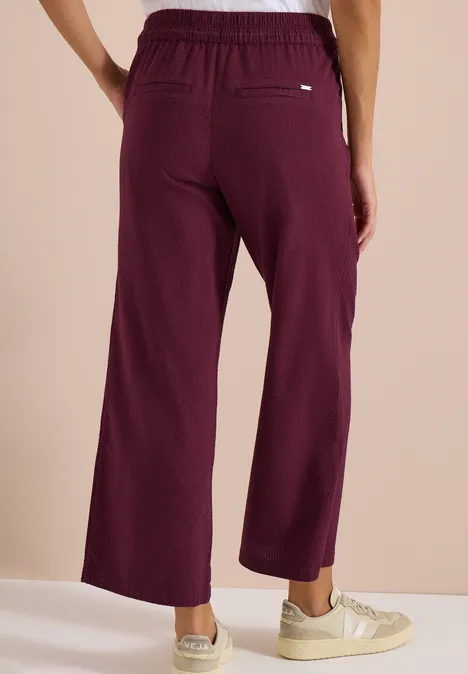 Achteraanzicht van een model in wijde bordeauxrode broek met elastische taille.