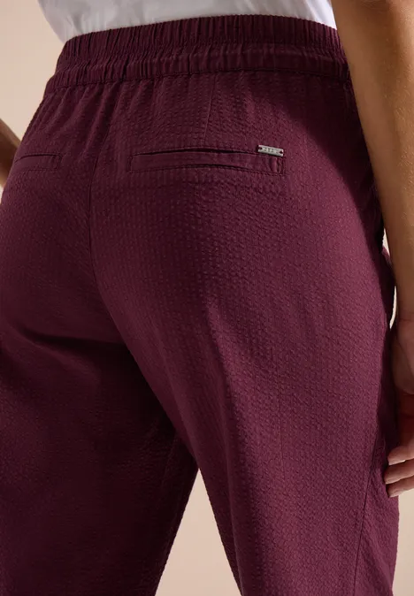 Achteraanzicht van iemand in bordeauxroze, gestructureerde broek met elastische taille en ritszak.