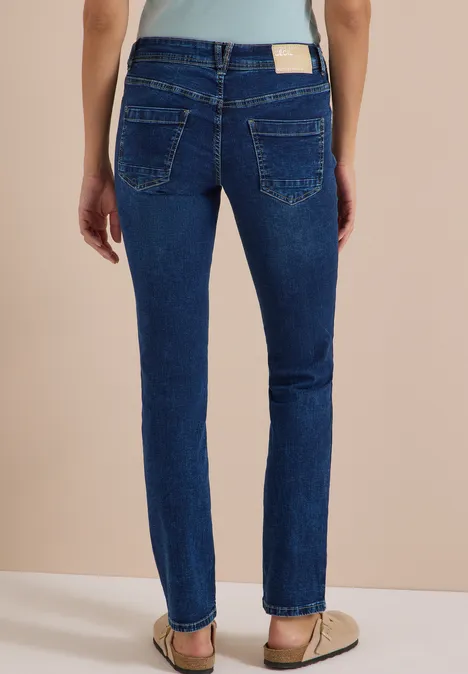 Mid Waist Straight Leg Jeans im Casual Fit mid blue used wash Frau trägt dunkelblaue Jeans von hinten, gerade geschnitten, dazu flache Sandalen.