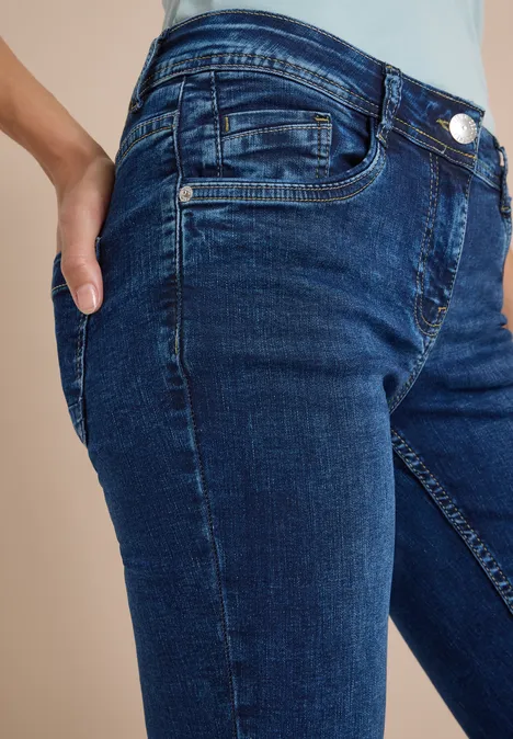 Mid Waist Straight Leg Jeans im Casual Fit mid blue used wash Seitliche Nahaufnahme einer Person in dunklen Jeans mit Hand in der Hosentasche.