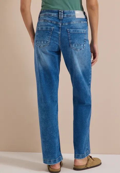 High Waist Wide Leg Jeans im Loose Fit mid blue wash Rückansicht einer Person in lässigen blauen Jeans und hellgrünem T-Shirt, vor beigem Hintergrund, mit braunen Schuhen.