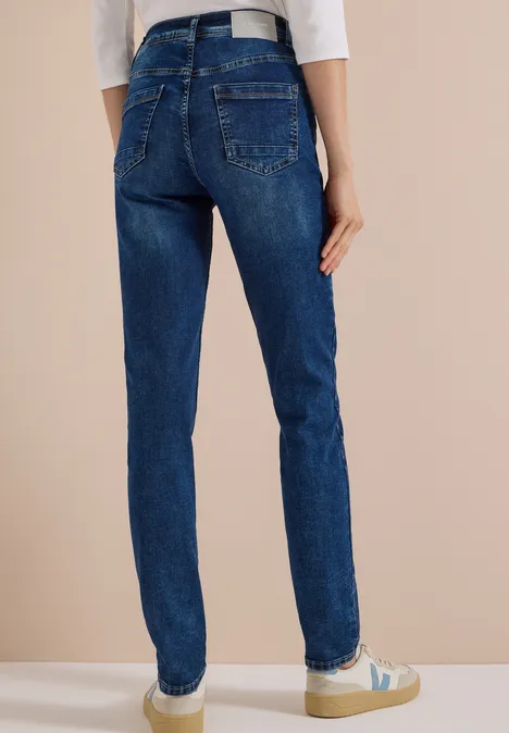 Vrouw van achteren in donkerblauwe jeans, witte riem en sneakers.