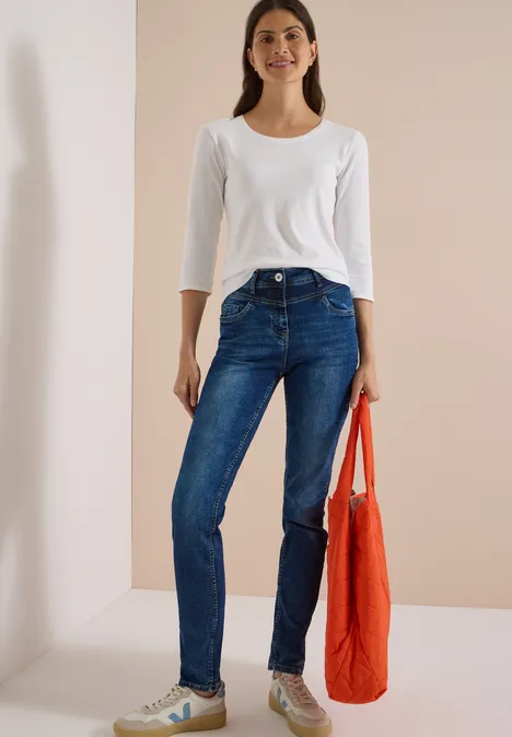Vrouw in wit shirt en blauwe spijkerbroek, met een oranje stoffen tas.