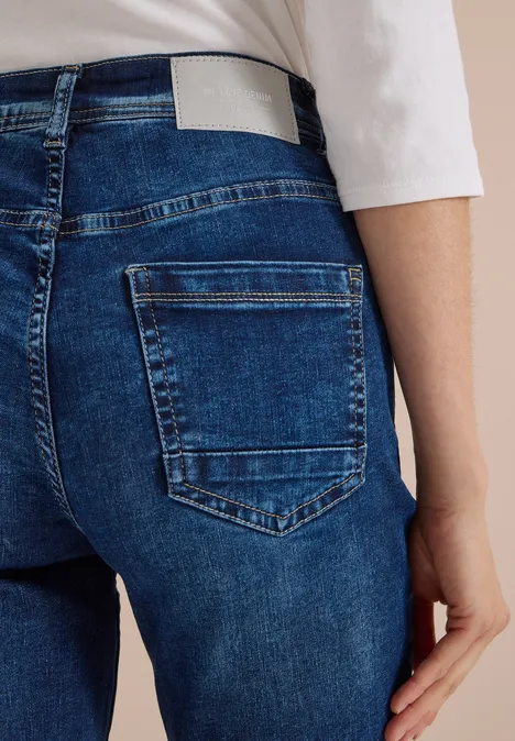 Achteraanzicht van persoon in blauwe jeans met achterzak en wit shirt, hand langs het lichaam.