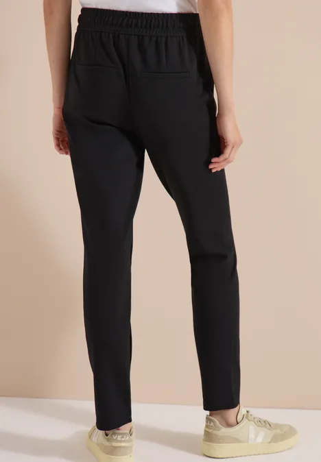 Strakke zwarte broek met elastische taille, gecombineerd met beige sneakers.