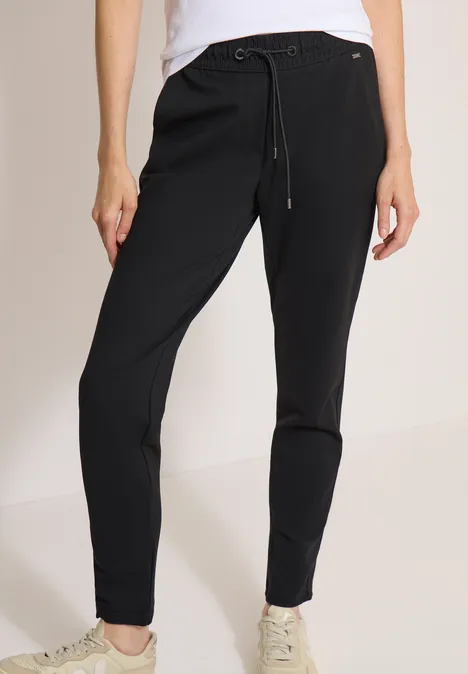 Vrouw draagt zwarte joggingbroek met trekkoord en witte sneakers.