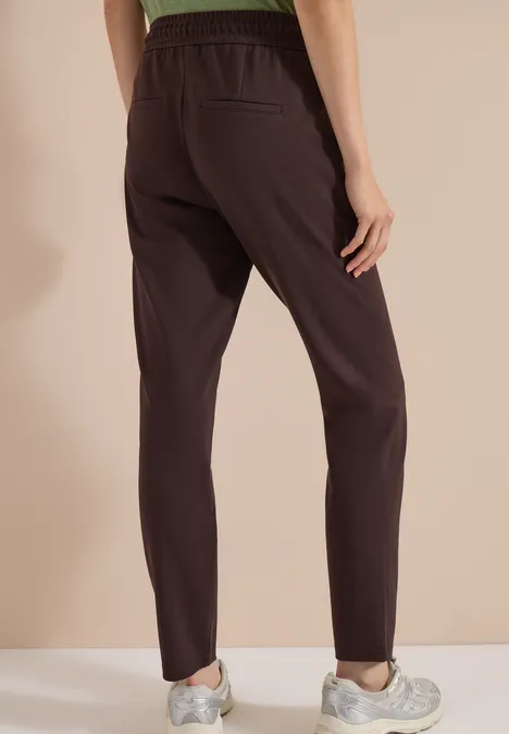Vue de dos d'une personne portant un pantalon marron foncé, taille élastique et baskets blanches.