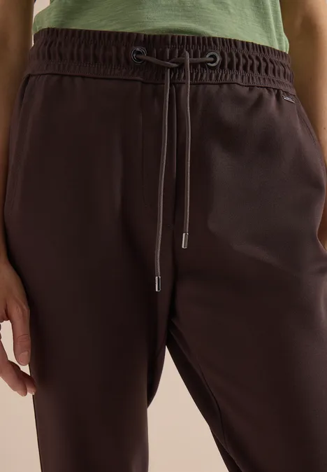 Gros plan sur un pantalon de jogging marron foncé à cordon, porté avec un haut vert.