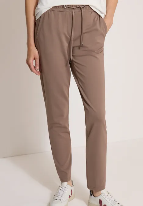 Jambes d’une personne portant un pantalon marron à cordon de serrage et des baskets blanches.