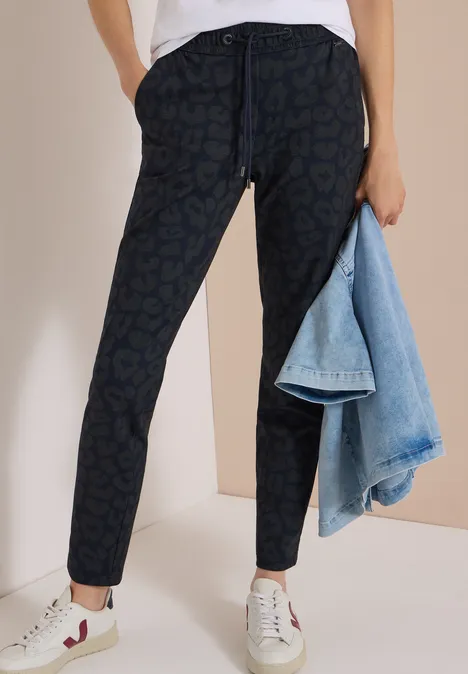Mid Waist Slim Leg Hose im Casual Fit dark navy blue Dunkle Jogginghose mit dezentem Print, weiße Sneaker und hellblaue Jeansjacke als Accessoire.