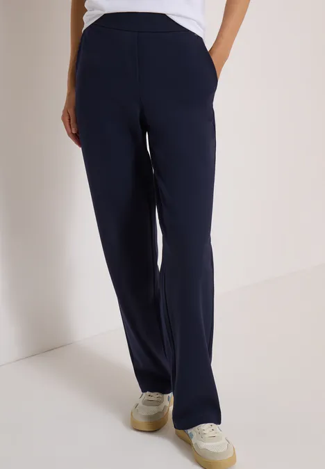 Dunkelblaue, gerade geschnittene Hose mit seitlichen Taschen, kombiniert mit weißen Sneakers.