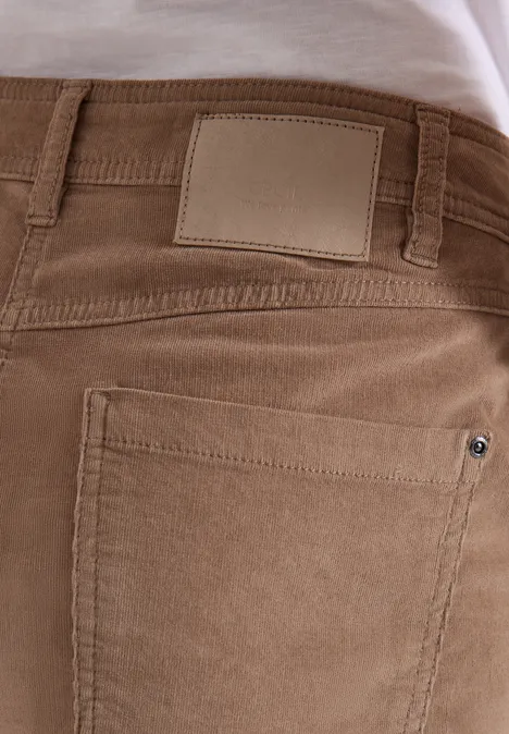 Nahaufnahme einer Person von hinten in hellbrauner Cordhose mit hinterer Tasche und Lederetikett am Bund.